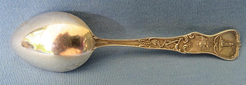 Souvenir Mining Spoon Wilkes-Barre Reverse.JPG - SOUVENIR MINING SPOON WILKES-BARRE PA - Sterling silver souvenir demitassespoon, 4 in. long, bowl engraved with colliery buildings and marked WILKES-BARRE, handle marked with image of William Penn and Liberty Bell with Pennsylvania, reverse marked Sterling and maker’s mark of Mechanics Sterling Co. (Attleboro, MA 1896 - ?), reverse handle marked with pick and shovel along with state seal  [Wilkes-Barre is in the center of the Wyoming Valley anthracite coal region in northeastern Pennsylvania.  Founded in 1769, it was originally named Wyoming but renamed later in honor of two British members of parliament, John Wilkes and Col. Issac Barre, who defended the American colonies in parliamentary debates.  In 1818, Wilkes-Barre was incorporated as a borough, with a city charter following in 1871.  Coal mining was the most important element of the city’s economy.   Hundreds of thousands of immigrants flocked to the city; they were seeking jobs in the numerous mines and collieries that sprang up.  Wilkes-Barre’s population exploded as the city became a center of supply to support these mines.  In 1914 employment at the anthracite mines reached a maximum of 180,000 workers.  Anthracite production peaked in 1917 at over 100 million tons with 776 mines in operation.  The anthracite industry went into steady decline after World War I.  The primary reason was competition from abundant supplies of lower cost oil and gas.  A large drop in anthracite production occurred during the Depression with only a small bounce-back during World War II.  The earlier downward trend continued after the War.  In 1959, The Knox Mine near Wilkes-Barre broke through the bottom of the Susquehanna River, flooding the underground mines and ending deep coal  production in the area.]